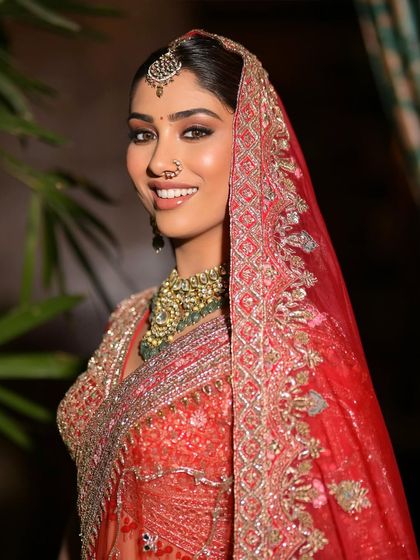A close-up of a model's smiling face, framed by a red dupatta and a beautiful green necklace set.