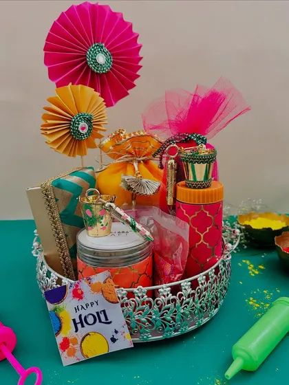 An elegant silver bowl holding a curated Holi hamper. This option includes colorful jars, potlis, and a pichkari, showing that Holi gifts can be both fun and sophisticated.