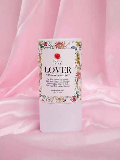 The perfume's cylindrical packaging shot against a pink satin background, focusing on the branding and design.