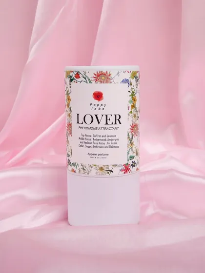 The perfume's cylindrical packaging shot against a pink satin background, focusing on the branding and design.