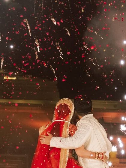 A beautiful, candid moment of the couple embracing during their varmala ceremony, framed by a shower of rose petals and fireworks. These are the emotional peaks I aim to create.
