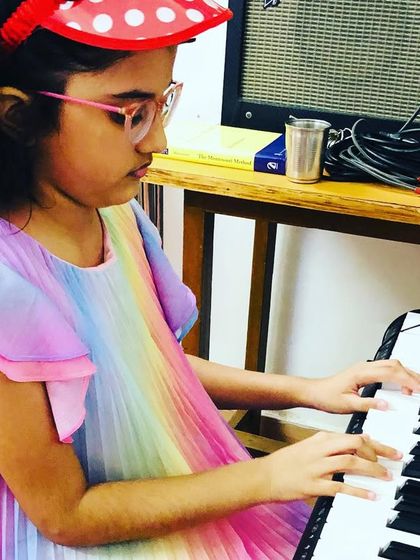 A young student, Sreesha, plays the keyboard during her class. Her colorful dress matches the joyful atmosphere of learning music at the Gurukul.
