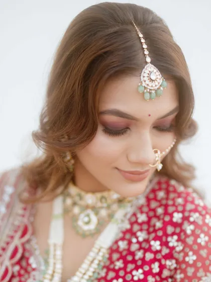 A close-up on the bride's makeup for her pheras. The focus is on her flawless skin and the deep red eyeshadow that complements her traditional red and green lehenga.
