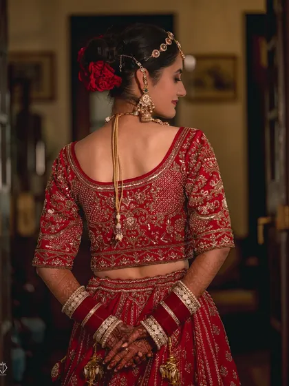 A portrait focusing on the beautiful details of the back of the bride's blouse and her hairstyle, adorned with a red rose. Every angle of the bridal look is important.
