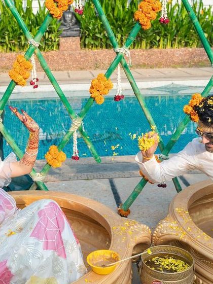A playful moment from a poolside Haldi ceremony, where the couple splashes each other with turmeric water in large brass urlis.