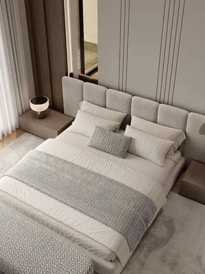An overhead view of a bedroom with a textured grey bed and bench. The wooden floor and large windows create a warm and inviting space.