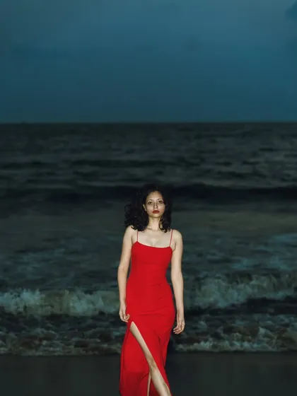 A full-length shot showing the elegant red dress against the vast, dark ocean. It's a very dramatic and lonely, yet powerful, scene.