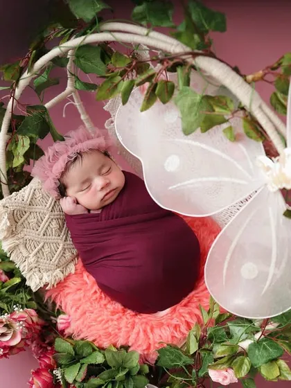 A touch of fairytale magic with this butterfly-themed setup. The baby is swaddled in a rich magenta wrap, sleeping in a floral hoop adorned with delicate, translucent wings.