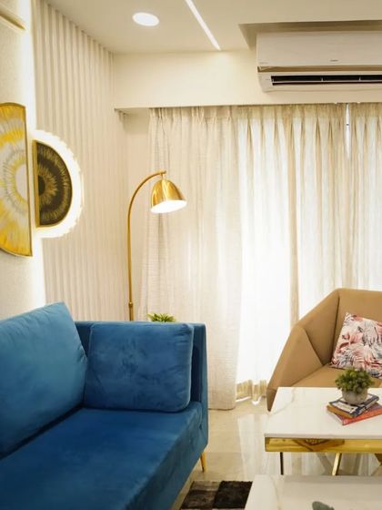 A cozy corner in a modern living room. The combination of a vibrant blue sofa, a neutral armchair, and a golden floor lamp creates a perfect spot for reading or relaxing.