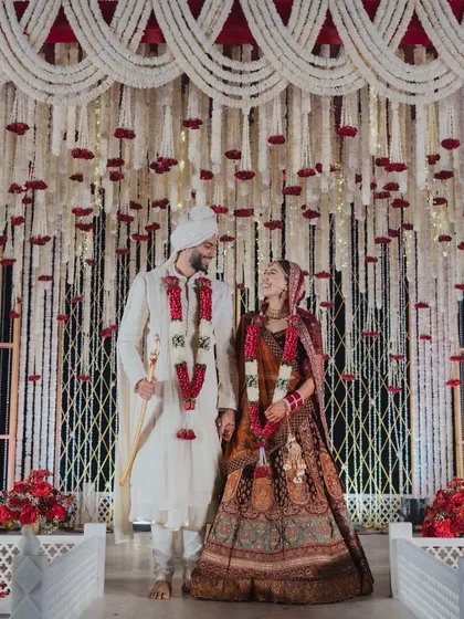 A beautiful shot of the couple framed by the intricate floral backdrop. The cascading mogra strings and red roses create a sense of depth and texture.