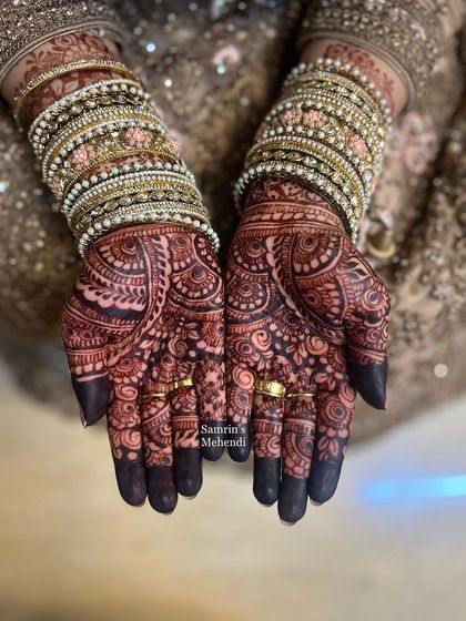 A beautiful shot of the final stain, adorned with sparkling bangles. The deep color on the fingertips and palms is the hallmark of a classic bridal mehendi.