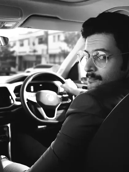 A black and white photograph of actor Ali Fazal in the driver's seat. The over-the-shoulder perspective makes the viewer feel like they are part of the scene, creating an engaging and personal portrait.