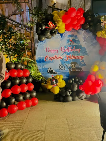 A pirate-themed birthday for 'Captain Shivaay'. The decor includes a custom backdrop with a pirate ship and a balloon arch in red, black, and yellow.