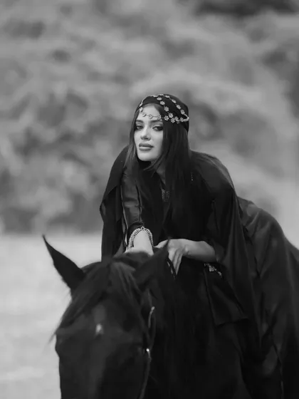 A close-up black and white portrait of a model on horseback, capturing a look of serene confidence.