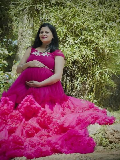 A serene portrait of a mom-to-be seated in a garden. The layers of her pink gown spread around her, creating a beautiful composition against the natural textures of the rocks and bamboo.