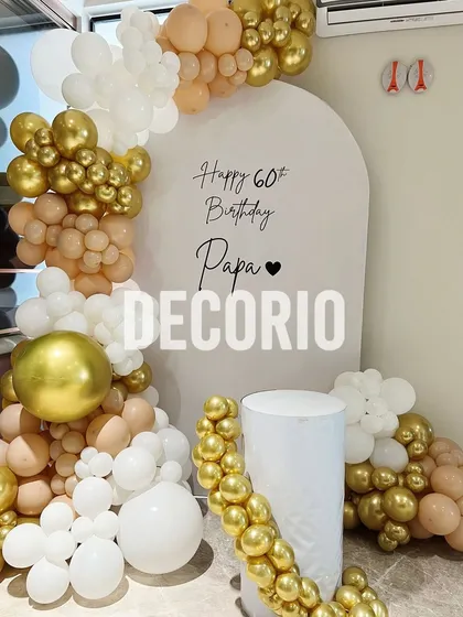 A heartfelt 60th birthday surprise for 'Papa'. This elegant setup includes a personalized white arched backdrop and a beautiful balloon garland in nude, white, and chrome gold tones.