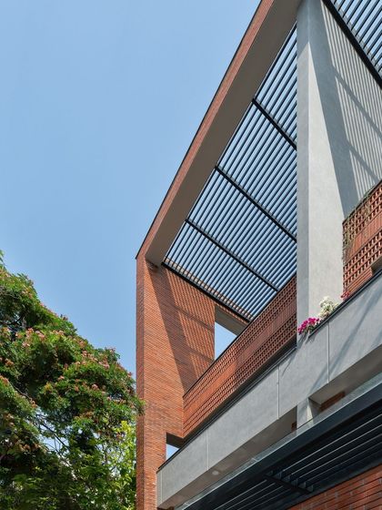 This apartment facade features a combination of exposed brick and a slatted pergola roof. These elements frame the sky and create dynamic shadows, adding texture and depth to the building's exterior.