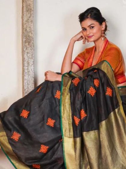 A black linen saree with bright orange embroidered motifs. The pop of color adds a playful touch to this elegant and comfortable saree.