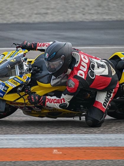 A rider on a yellow Ducati showing incredible body posture and control, hanging off the bike to maintain speed through the corner.