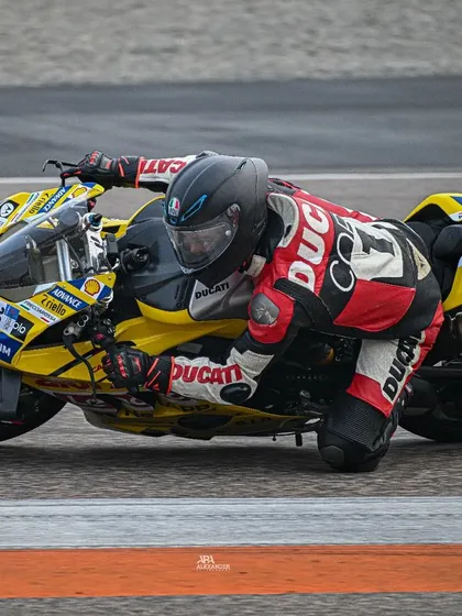 A rider on a yellow Ducati showing incredible body posture and control, hanging off the bike to maintain speed through the corner.