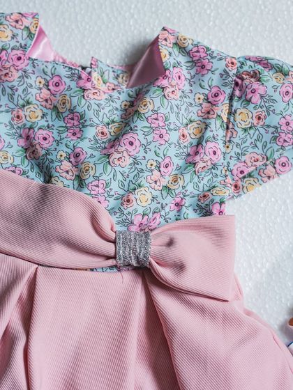 This image highlights the beautiful contrast between the floral puff-sleeve bodice and the solid pink pleated skirt. The silver buckle on the bow adds a touch of modern sparkle.