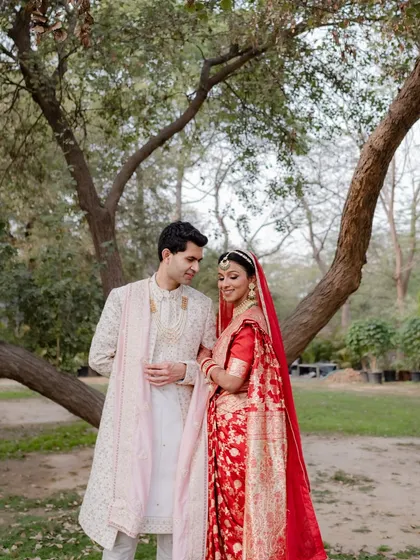A beautiful couple portrait. Her traditional red saree is complemented by makeup that enhances her features without being overpowering, perfect for an outdoor setting.
