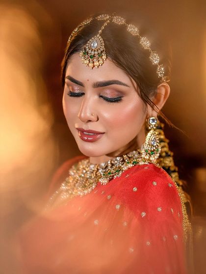 A close-up portrait with soft, glowing light, highlighting the warm tones of the red bridal lehenga look.