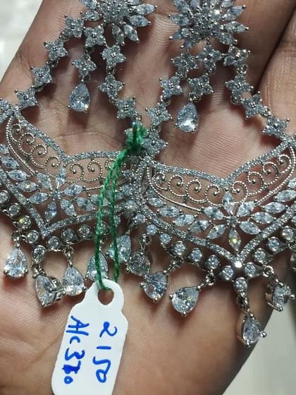 A pair of elegant silver-polished American Diamond earrings with a delicate, flowing design.