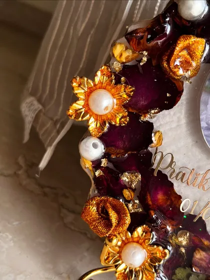A close-up shot of the decorative elements on a budget-friendly photo frame. The golden flowers with pearl centers add a touch of glamour to the preserved rose petals.