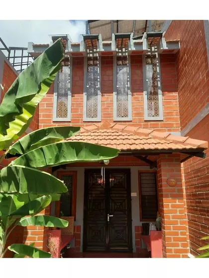 The entrance to the Anjali and Anshuman residence, where a banana plant frames the view of the exposed brick facade and decorative jaali windows.