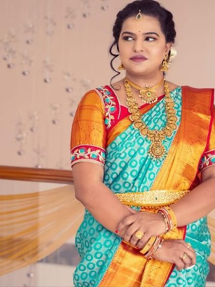A solo portrait showcasing the traditional look. The turquoise and orange saree is complemented by a soft smokey eye and a neutral lip.