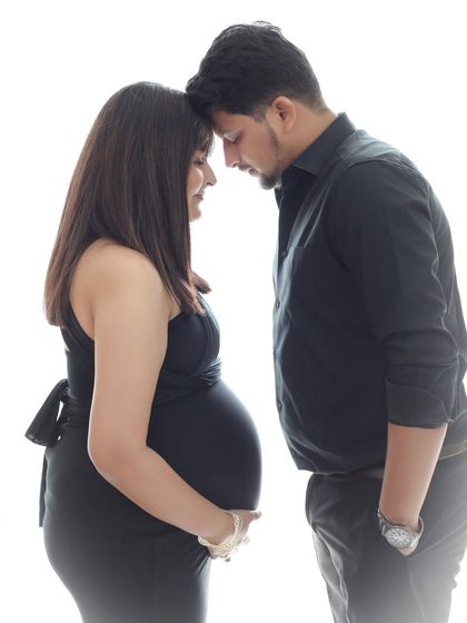 A tender moment between partners, captured in a simple, high-contrast setting. The focus is entirely on their connection and the baby they are waiting for.