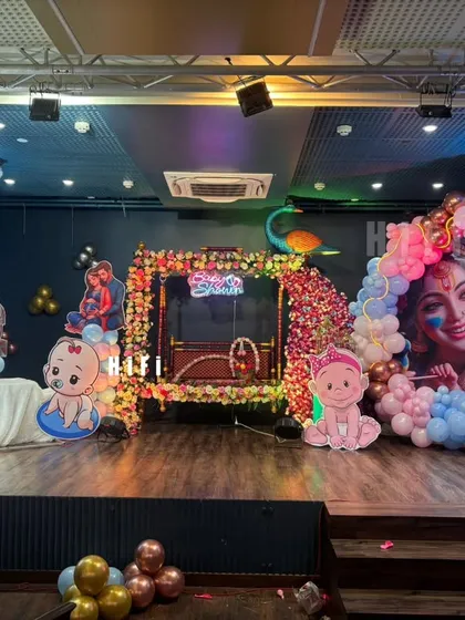 A grand stage setup for a baby shower or naming ceremony. This decor features a large moon prop, a decorated cradle, and multiple character cutouts with a Krishna theme.
