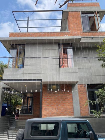 A frontal view of Ramya and Madhu's residence, showcasing the clean lines and material contrast. The design balances modern aesthetics with the warmth of natural brick.