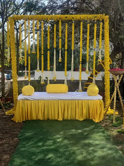 A classic Haldi ceremony setup, radiating pure joy and tradition. The backdrop is crafted entirely from bright yellow marigold garlands, creating a perfect, sun-kissed space for this happy occasion.