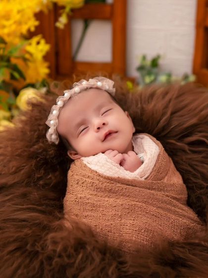A peacefully sleeping newborn, swaddled in earthy brown tones and nestled in a soft fur basket. This portrait showcases our classic posing style, ensuring the baby is comfortable, safe, and beautifully framed.