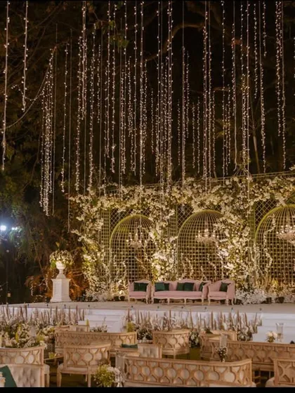 A breathtaking night view of a reception stage, with thousands of fairy lights cascading from the trees above. The design creates a magical, starry-night effect over the entire seating area.