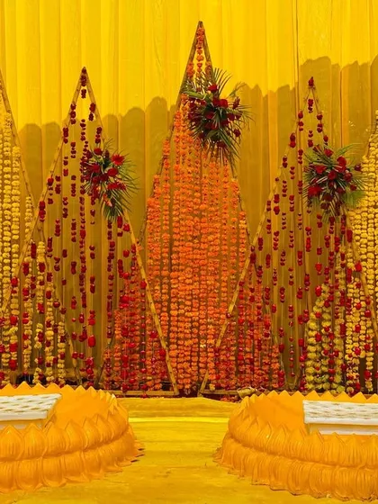 A traditional Haldi seating area, with a backdrop made of marigold and rose petal strings in geometric patterns.