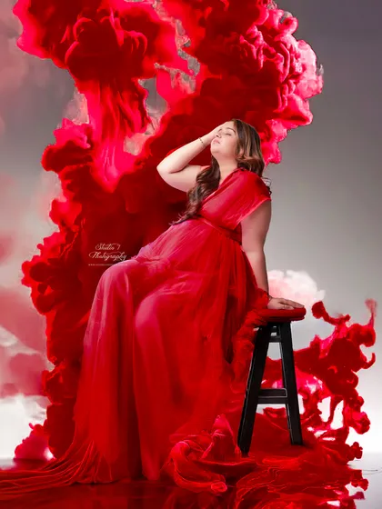 This creative studio shot uses a red smoke effect to add drama and artistry. The vibrant color beautifully contrasts with the expecting mother's serene expression.