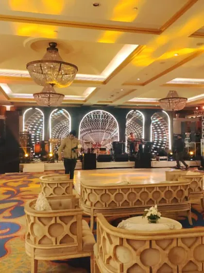 A wide view of a Sangeet hall, showing the relationship between the comfortable, carved wood lounge seating in the foreground and the dynamic LED stage in the background.