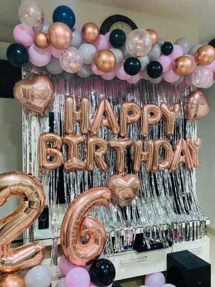 A stylish 26th birthday backdrop with a silver tinsel curtain and a balloon garland in pink, black, and rose gold.