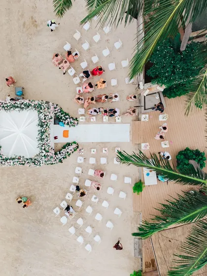 An aerial drone shot of a beach wedding ceremony in Thailand. This perspective shows the beautiful layout of the event, with the guests seated on the sand and the elegant mandap positioned right by the water's edge.