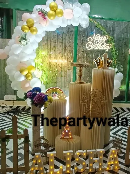 A whimsical ring decoration with white and gold balloons against a patterned floor. The picket fence and light-up name add a charming touch.