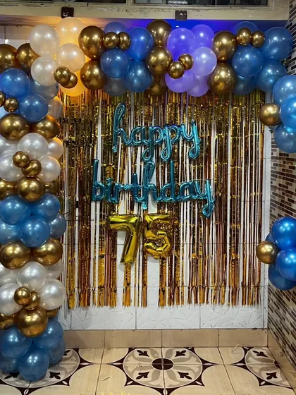 A simple yet effective L-shaped balloon arch is great for home parties. This one, for a 75th birthday, uses a gold, blue, and white color scheme with a foil curtain backdrop.