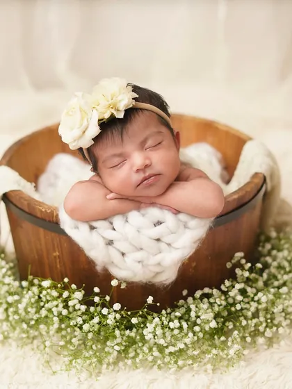 A frontal view of the baby in the wooden bucket, showcasing her sweet, sleeping face and floral headband. I carefully pose babies to ensure they are both safe and look angelic.