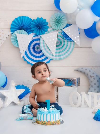 Surrounded by a sea of blue and white, this one-year-old is about to get his first taste of birthday cake. The anticipation is just adorable.