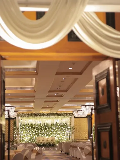A glimpse into the Nikah ceremony hall through the elegantly decorated entrance, showing the beautiful white floral stage in the distance.