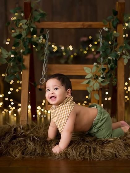 Exploring the set. This wider shot shows the baby crawling on a furry rug in front of a rustic wooden swing, surrounded by fairy lights.