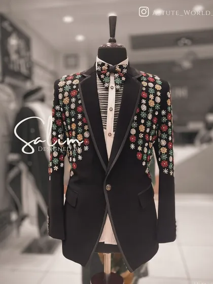 A black tuxedo jacket on a mannequin, adorned with colorful, beaded floral clusters on the shoulders. This is a vibrant and modern take on formalwear embellishment.