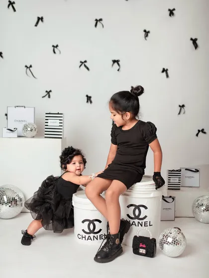 Big sister helps her little sister stand, a sweet moment of support amidst the high-fashion fun.